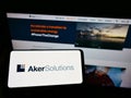 Person holding cellphone with logo of Norwegian engineering company Aker Solutions ASA on screen in front of webpage.
