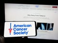 Person holding cellphone with logo of organization American Cancer Society (ACS) on screen in front of webpage.