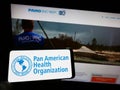 Person holding cellphone with logo of Pan American Health Organization (PAHO) on screen in front of webpage. Royalty Free Stock Photo