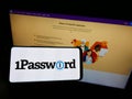 Person holding cellphone with logo of password manager company AgileBits Inc. (1Password) on screen in front of webpage.