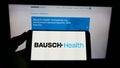 Person holding cellphone with logo of pharmaceutical company Bausch Health Companies Inc. on screen in front of webpage. Royalty Free Stock Photo