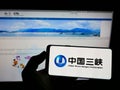 Person holding cellphone with logo of power company China Three Gorges Corporation (CTG) on screen in front of webpage.