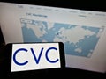 Person holding cellphone with logo of private equity firm CVC Capital Partners on screen in front of company web page.