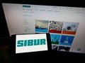 Person holding cellphone with logo of Russian petrochemicals company SIBUR Holding PJSC on screen in front of webpage.