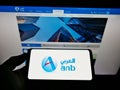 Person holding cellphone with logo of Saudi Arabian financial company Arab National Bank on screen in front of webpage.
