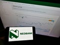 Person holding cellphone with logo of South African bank Nedbank Group Limited on screen in front of website with chart.