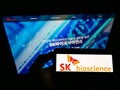 Person holding cellphone with logo of South Korean biological company SK Bioscience on screen in front of business website.