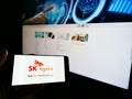 Person holding cellphone with logo of South Korean semiconductor manufacturer SK hynix Inc. on screen in front of web page.