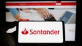 Person holding cellphone with logo of Spanish banking company Banco Santander SA on screen in front of business webpage.