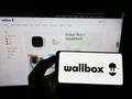 Person holding cellphone with logo of Spanish energy company Wallbox Charger S.L. on screen in front of business webpage.