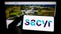 Person holding cellphone with logo of Spanish infrastructure company Sacyr S.A. on screen in front of business web page.