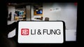 Person holding cellphone with logo of supply chain management company Li Fung Limited on screen in front of webpage.