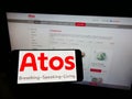 Person holding cellphone with logo of Swedish medical technology company Atos Medical AB on screen in front of webpage.