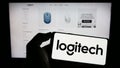 Person holding cellphone with logo of Swiss company Logitech International S.A. on screen in front of business webpage.