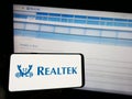 Person holding cellphone with logo of Taiwanese company Realtek Semiconductor Corp. on screen in front of webpage. Royalty Free Stock Photo