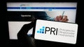 Person holding cellphone with logo of UN Principles for Responsible Investment (PRI) on screen in front of webpage.