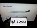Person holding cellphone with logo of US aerospace company Boom Technology Inc. (Supersonic) on screen with web page.
