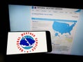 Person holding cellphone with logo of US agency National Weather Service (NWS) on screen in front of webpage.