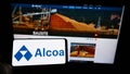 Person holding cellphone with logo of US aluminium company Alcoa Corporation on screen in front of business webpage. Royalty Free Stock Photo