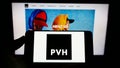 Person holding cellphone with logo of US clothing company PVH Corp. on screen in front of business webpage.