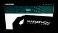 Person holding cellphone with logo of US company Marathon Digital Holdings Inc. on screen in front of business webpage.