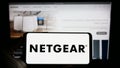 Person holding cellphone with logo of US computer networking company Netgear Inc. on screen in front of business webpage. Royalty Free Stock Photo