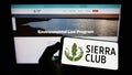 Person holding cellphone with logo of US environmental organization Sierra Club on screen in front of webpage.