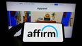 Person holding cellphone with logo of US financial technology company Affirm Holdings Inc. on screen in front of web page.