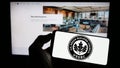 Person holding cellphone with logo of US Green Building Council (USGBC) on screen in front of webpage.