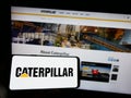 Person holding cellphone with logo of US heavy equipment company Caterpillar Inc. on screen in front of business webpage.