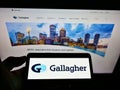 Person holding cellphone with logo of US insurance company Arthur J. Gallagher Co. on screen in front of business website.