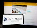 Person holding cellphone with logo of US insurance company Liberty Mutual Group on screen in front of business webpage.