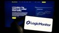 Person holding cellphone with logo of US monitoring company LogicMonitor Inc. on screen in front of business webpage.