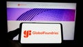 Person holding cellphone with logo of US semiconductor company GlobalFoundries Inc. (GF) on screen in front of webpage.