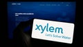 Person holding cellphone with logo of US water technology company Xylem Inc. on screen in front of business webpage.