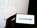 Person holding cellphone with logo of vaccine company CanSino Biologics Inc. (CanSinoBIO) on screen in front of webpage.