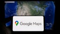 Person holding cellphone with logo of web mapping platform Google Maps on screen in front of webpage.