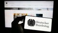 Person holding cellphone with seal of German federal parliament Bundestag on screen in front of webpage.