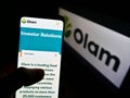 Person holding cellphone with web page of agribusiness company Olam International Ltd on screen in front of logo.