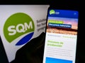 Person holding cellphone with web page of company Sociedad QuÃÂ­mica y Minera de Chile (SQM) on screen with logo.