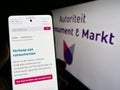 Person holding cellphone with web page of Dutch regulator Autoriteit Consument en Markt (ACM) on screen.