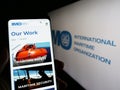 Person holding cellphone with web page of International Maritime Organization (IMO) on screen in front of logo.