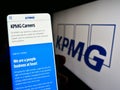Person holding cellphone with web page of professional services company KPMG on screen in front of logo.