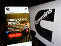 Person holding cellphone with web page of US manufacturing company Cummins Inc. on screen in front of logo.