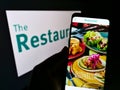 Person holding cellphone with webpage of British gastronomy company The Restaurant Group plc on screen with logo.
