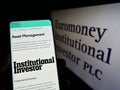 Person holding cellphone with webpage of company Euromoney Institutional Investor plc on screen with logo.