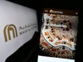 Person holding cellphone with webpage of Emirati company Majid Al Futtaim Group on screen in front of logo.