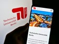 Person holding cellphone with webpage of German university Technische UniversitÃÂ¤t Berlin on screen in front of logo.