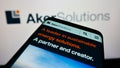 Person holding cellphone with webpage of Norwegian engineering company Aker Solutions ASA on screen with logo.