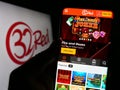 Person holding cellphone with webpage of online casino company 32Red Limited on screen in front of logo.